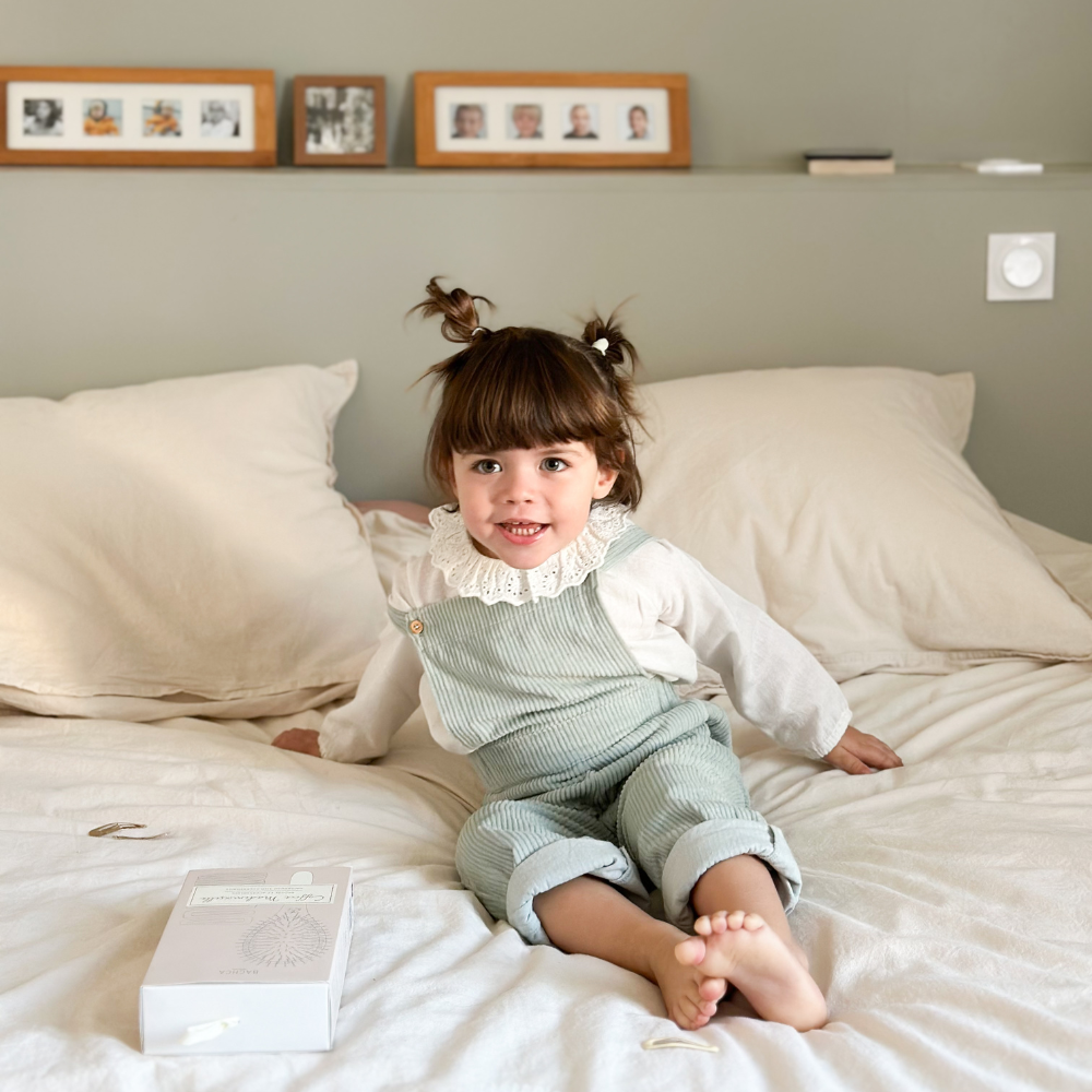 Petite fille sur un lit. Elle sourit à la caméra, on voit à côté d&