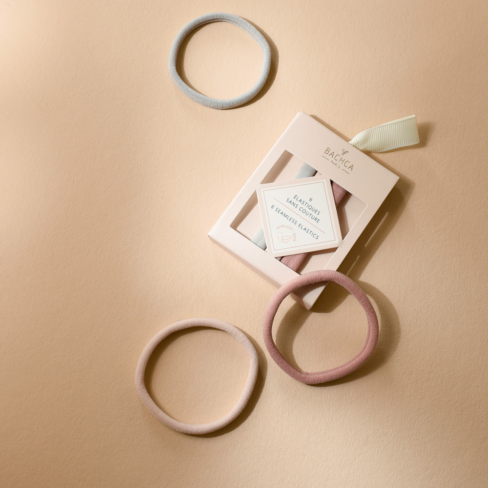 Boîte d’élastiques sans couture Bachca en tons pastel avec quatre élastiques disposés autour, photographiée sur une surface beige.