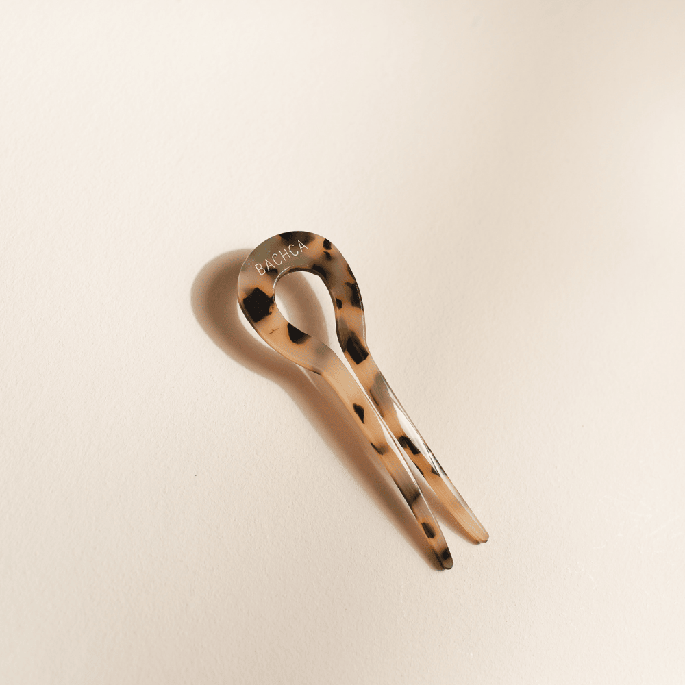 Épingle à chignon Bachca en acétate effet écaille, posée sur un fond beige avec ombre douce.