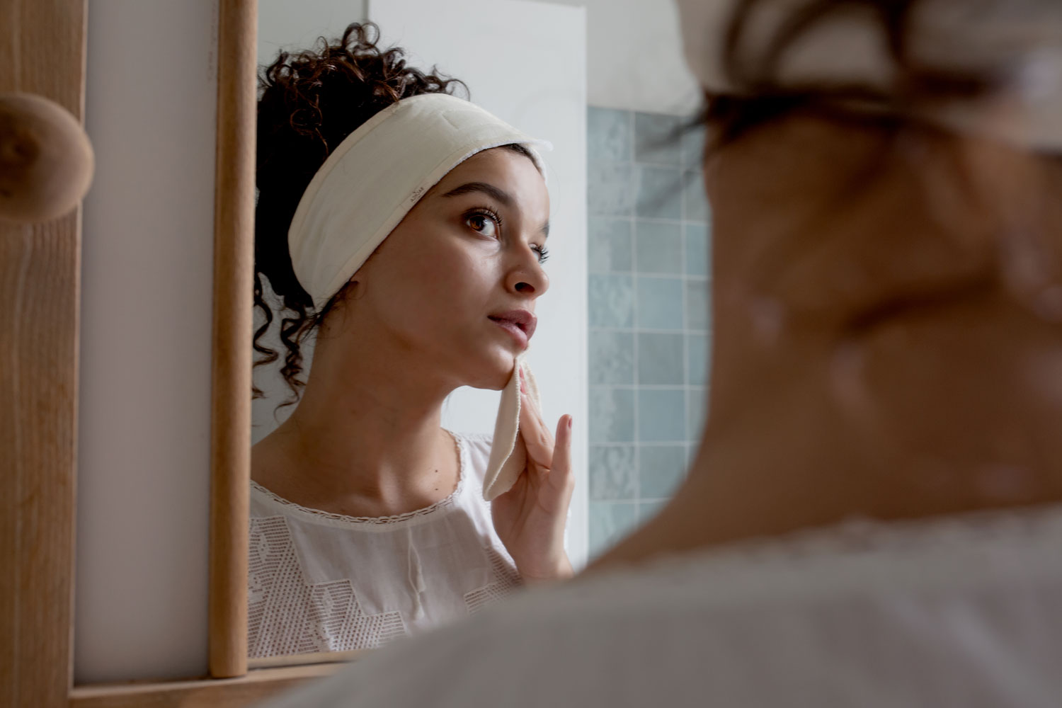 Femme portant un bandeau écru Bachca se démaquillant devant un miroir avec un coton lavable.