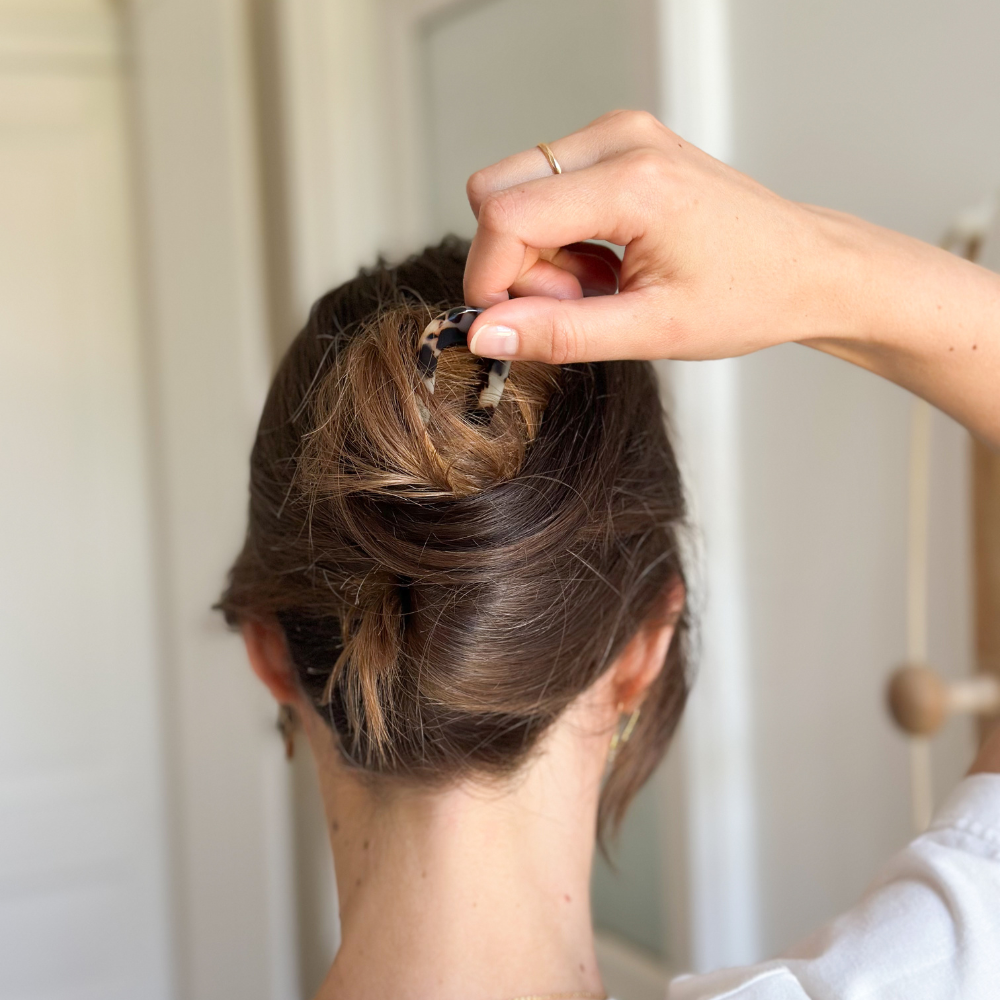 Femme de dos réalisant un chignon avec le pic chignon écaille Bachca, accessoire élégant en acétate de cellulose qui maintient les cheveux tout en apportant une touche sophistiquée à la coiffure.