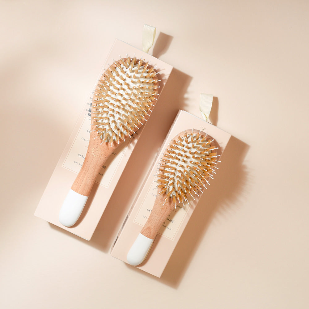 Grand et petit modèle de brosses Bachca démêlage & brillance, en bois de hêtre et poils de sanglier avec picots nylon, posées sur leurs étuis rosés.