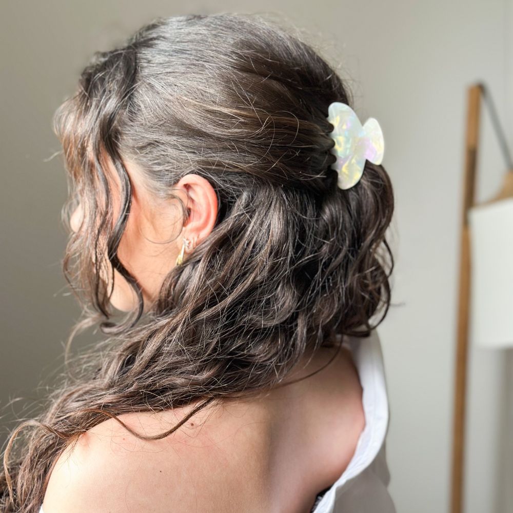Cheveux bouclés relevés avec grande pince nacrée Bachca, accessoire élégant au fini irisé.