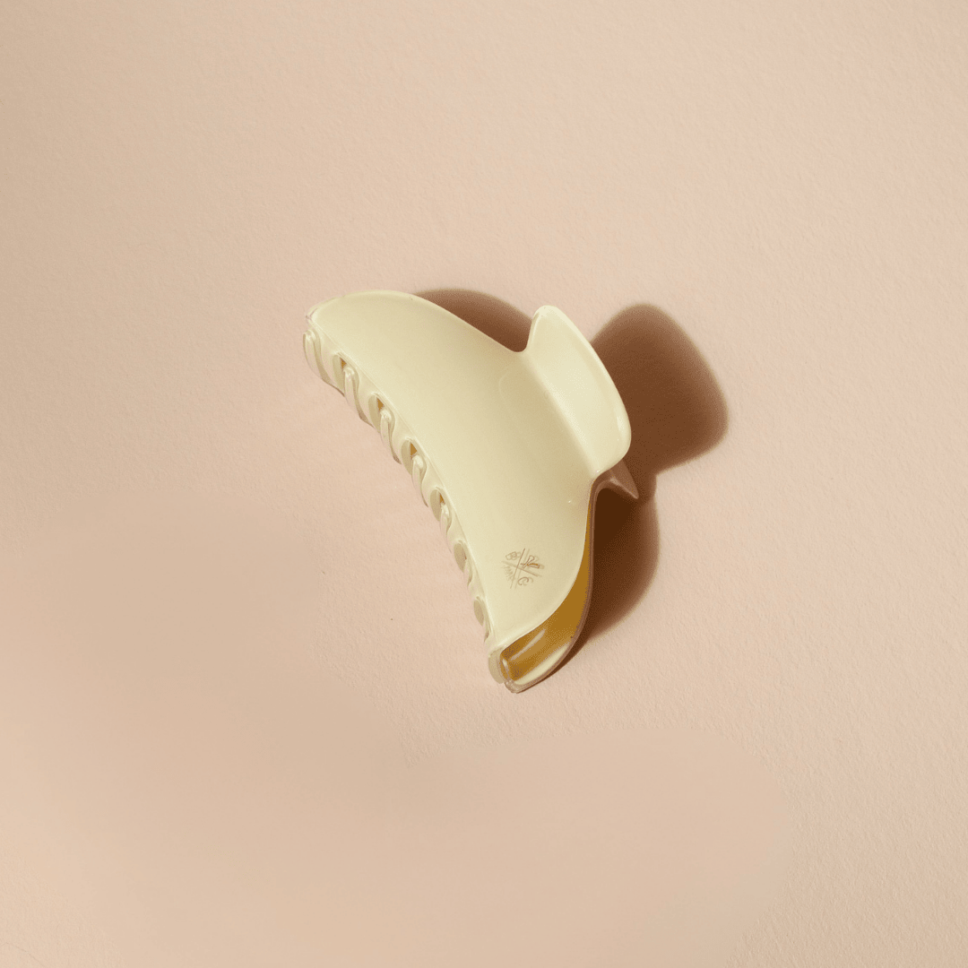 Grande pince à cheveux Bachca en acétate effet ivoire, vue de profil sur fond beige. Sa silhouette incurvée et ses larges dents sont mises en valeur par la lumière douce et l’ombre projetée.