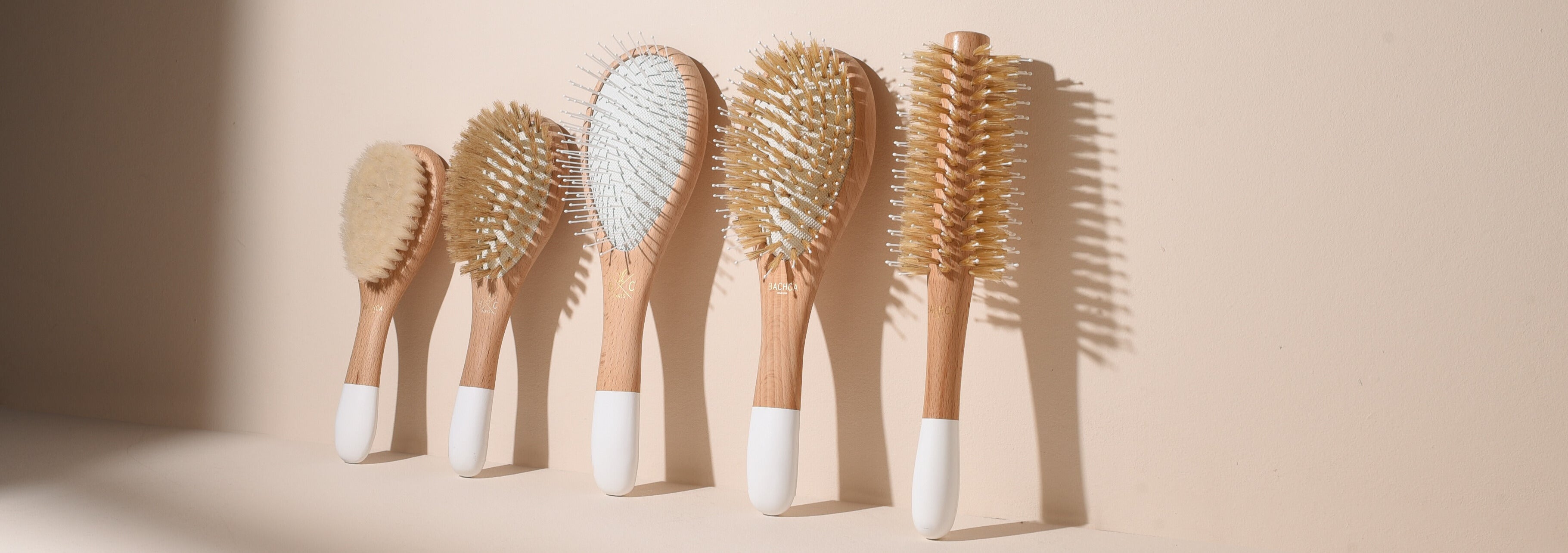 Collection de cinq brosses à cheveux Bachca sur fond rose pâle : brushing, brillance, volume, cheveux fins et brosse bébé en soie de chèvre.