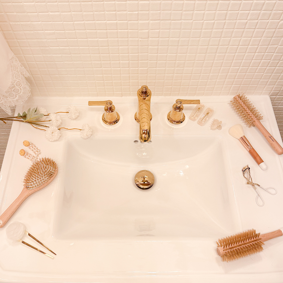 Brosses à cheveux et accessoires nacrés Bachca disposés autour d’un lavabo blanc à robinetterie dorée dans une salle de bain lumineuse.