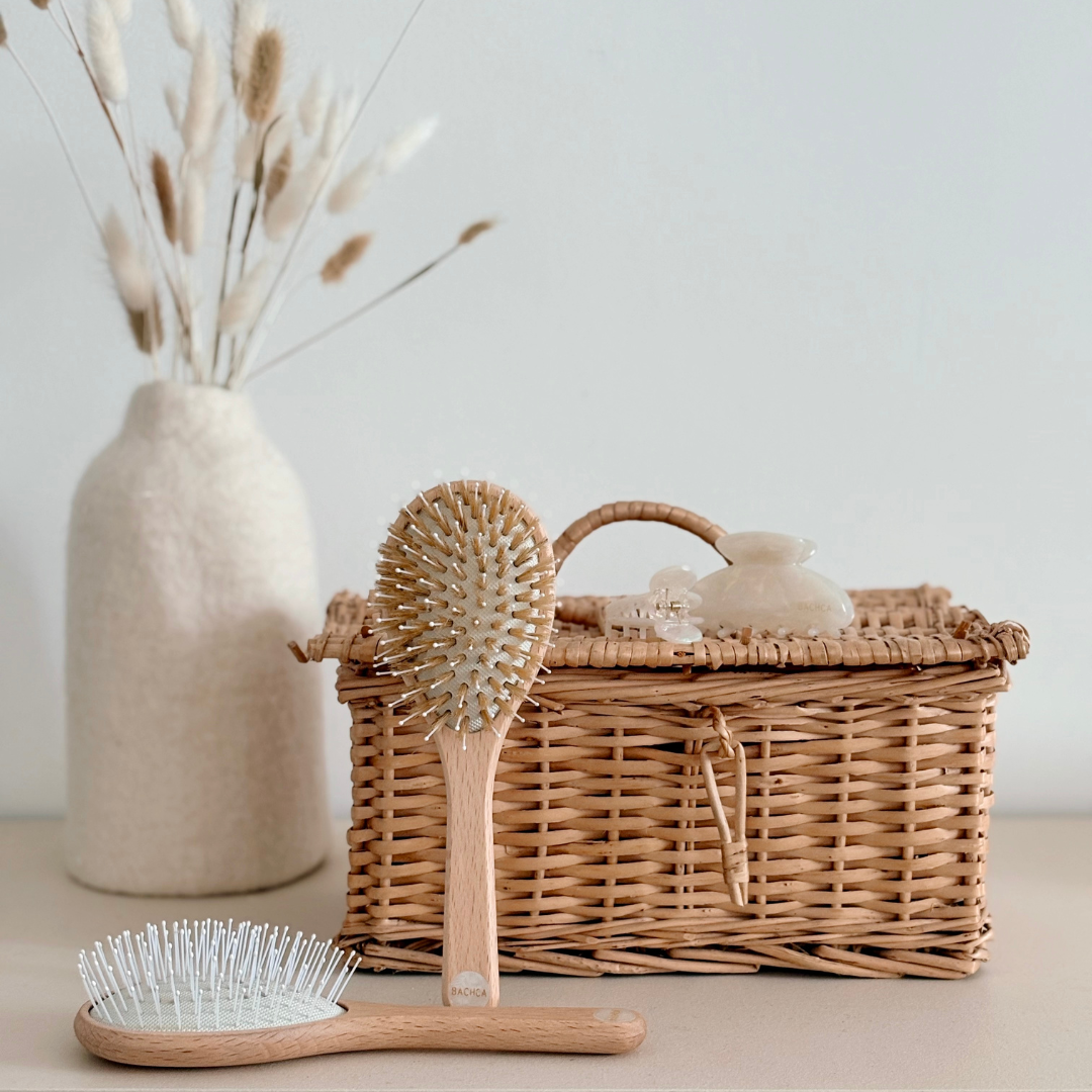 Deux brosses à cheveux made in France Bachca en bois devant un panier en osier et une pince en acétate.