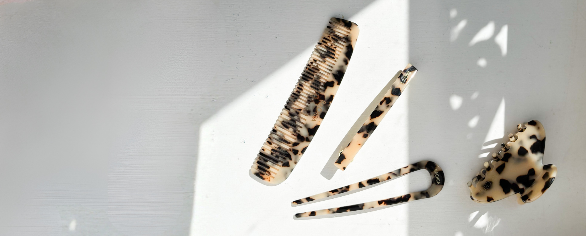 Quatre accessoires cheveux écailles, un peigne pour cheveux fins, un grand pic chignon, une grande pince et une barrette écailles. Les accessoires sont sur un fond blanc avec des ombres.