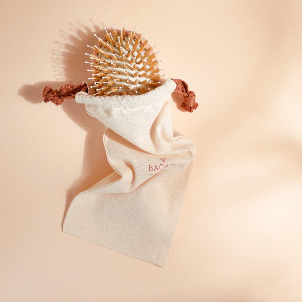 Brosse à cheveux Bachca en bois de hêtre avec picots nylon et sanglier, présentée dans son pochon en coton beige avec cordons terracotta, idéale pour le démêlage et la brillance.