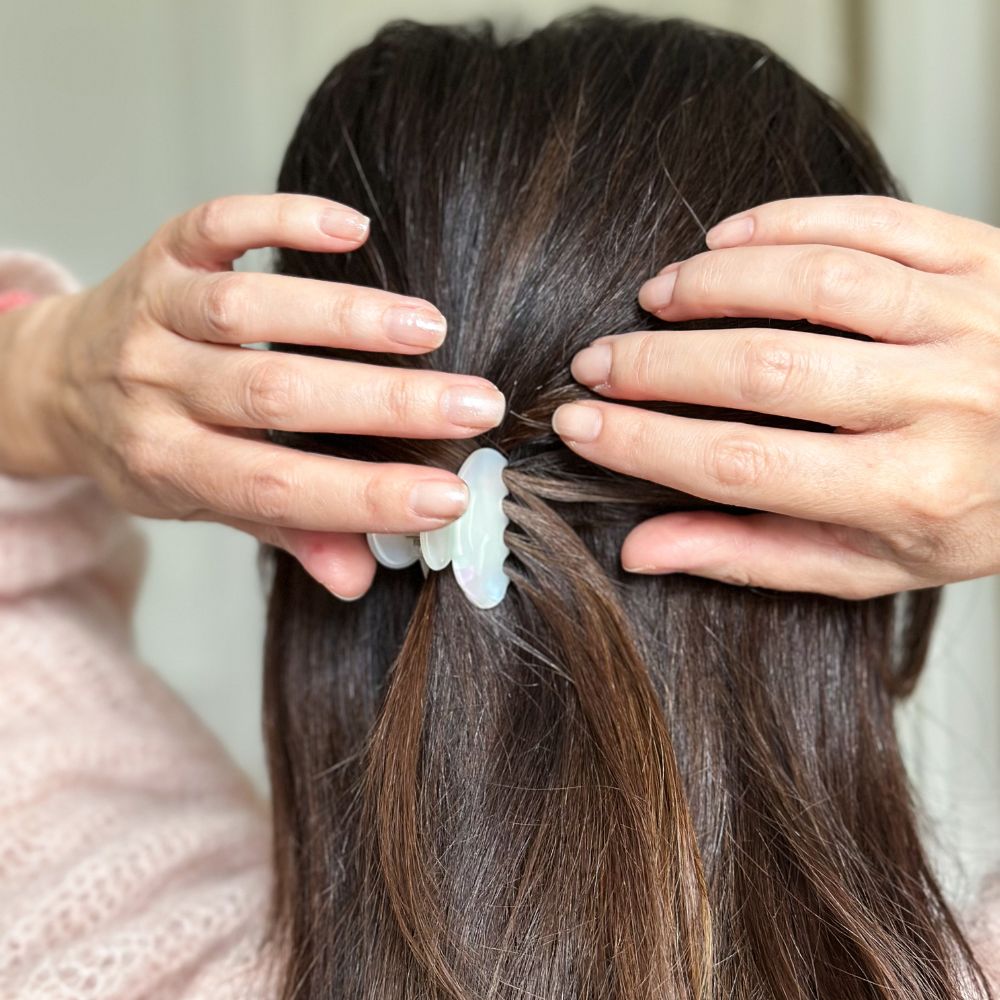 Cheveux bruns attachés à mi-hauteur avec une petite pince nacrée Bachca, geste délicat des mains.