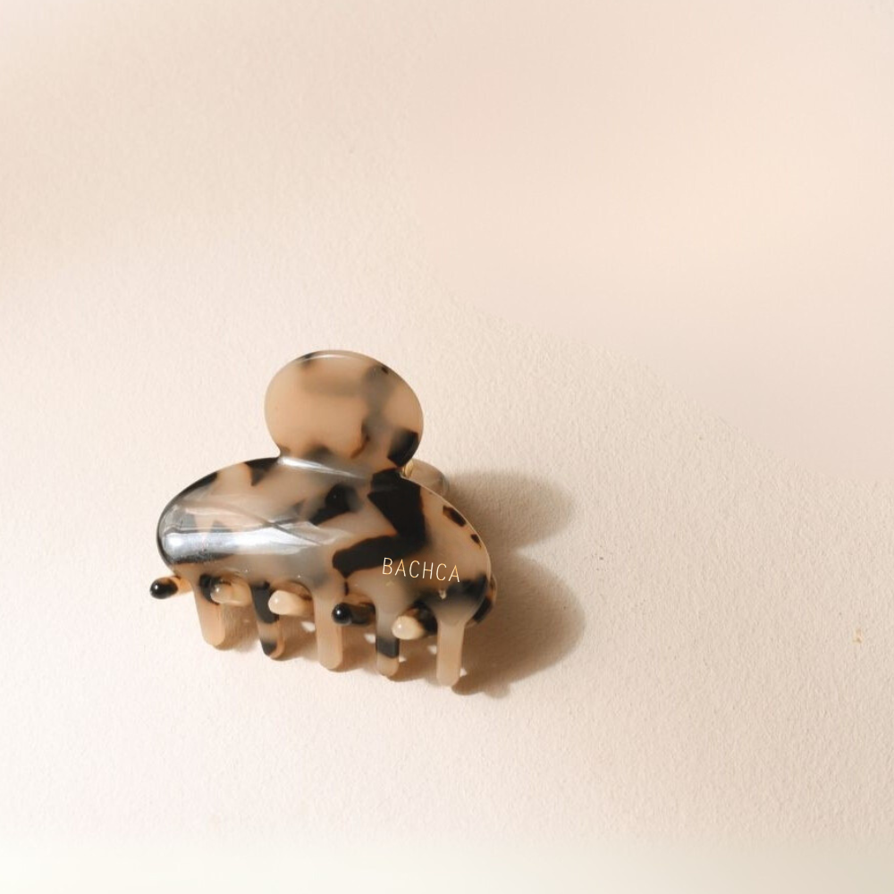 Petite pince à cheveux motif écaille de la marque Bachca, présentée sur fond rose pâle.