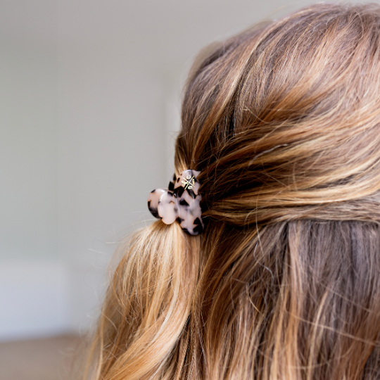 Zoom sur une demi-queue attachée avec une petite pince à cheveux motif écaille beige et noir, sur des cheveux châtain clair aux reflets dorés.