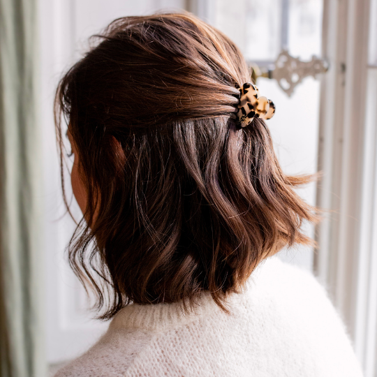 Vue arrière d’une femme aux cheveux châtain foncé coiffés en demi-queue maintenue par une petite pince à cheveux motif écaille, portée avec un pull écru en maille fine.