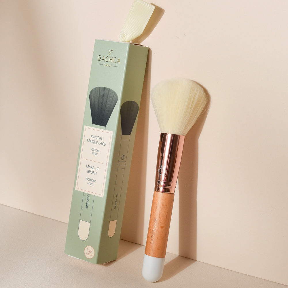 Pinceau poudre Bachca avec manche en bois naturel et virole rose doré, présenté avec son étui vert, idéal pour un maquillage du teint uniforme.
