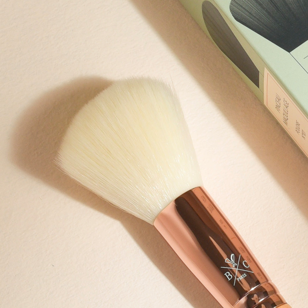 Pinceau poudre Bachca gros plan sur les poils ultra-doux et la bague rose gold, idéal pour appliquer uniformément la poudre sur le visage.