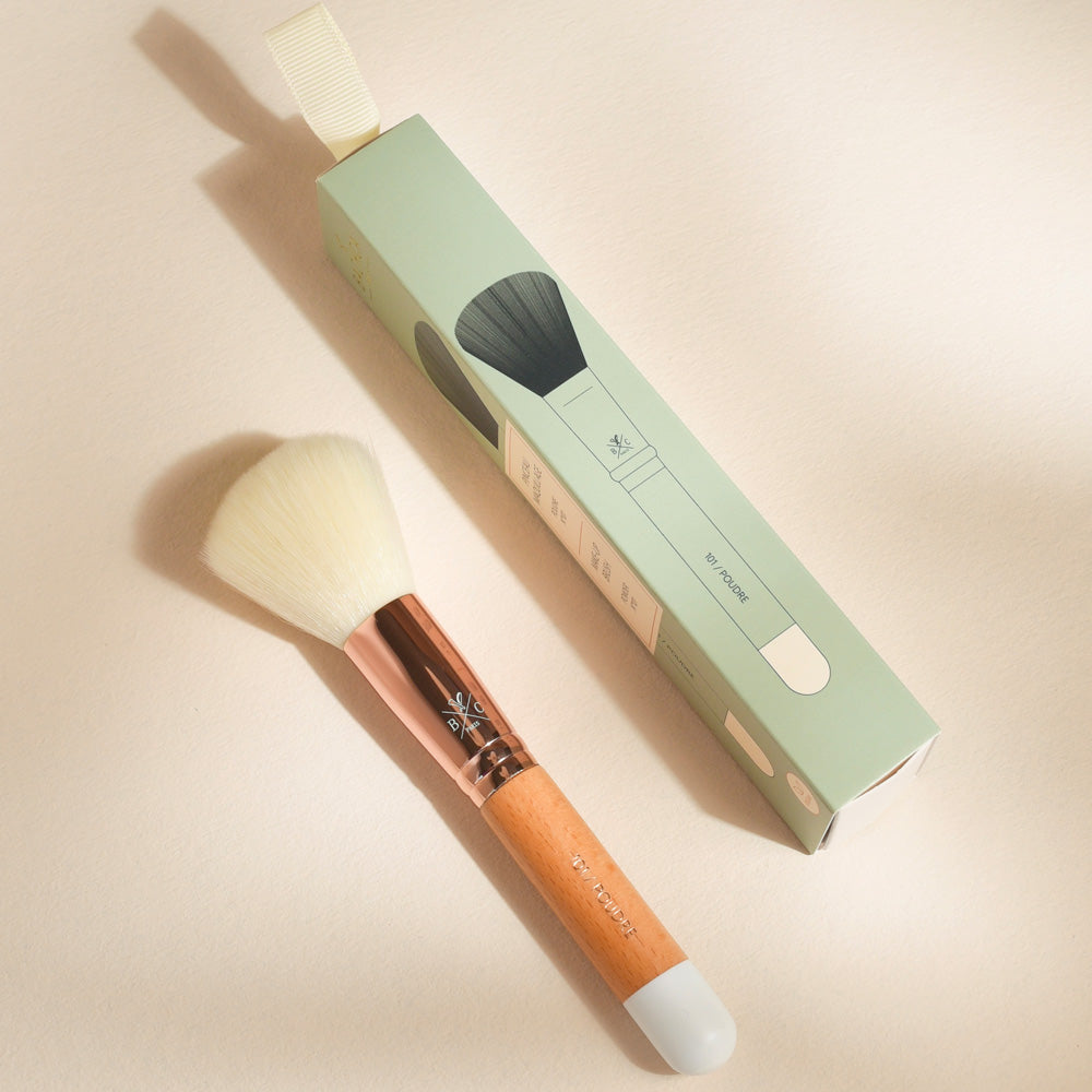 Pinceau poudre Bachca pour maquillage du teint avec manche en bois naturel et poils ultra-doux, présenté à côté de son étui vert élégant.