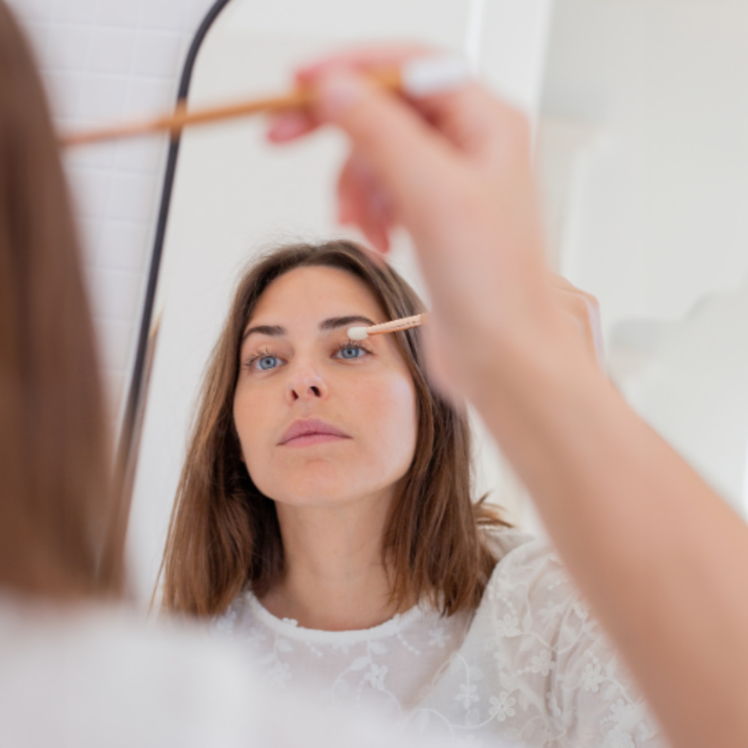 Femme appliquant du fard à paupières avec un pinceau yeux biseauté Bachca en bois, devant un miroir, dans une salle de bain lumineuse.