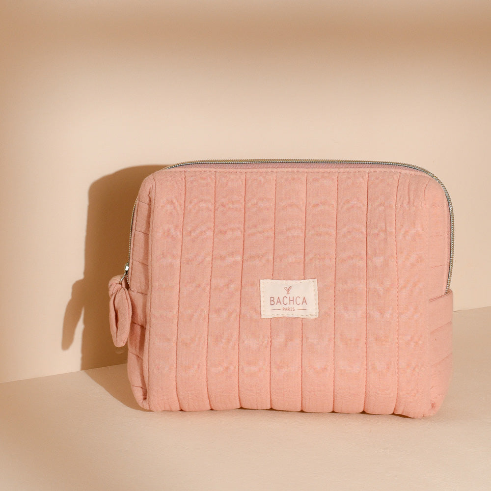 Trousse de toilette Bachca en coton matelassé rose poudré avec fermeture éclair, posée sur fond nude.