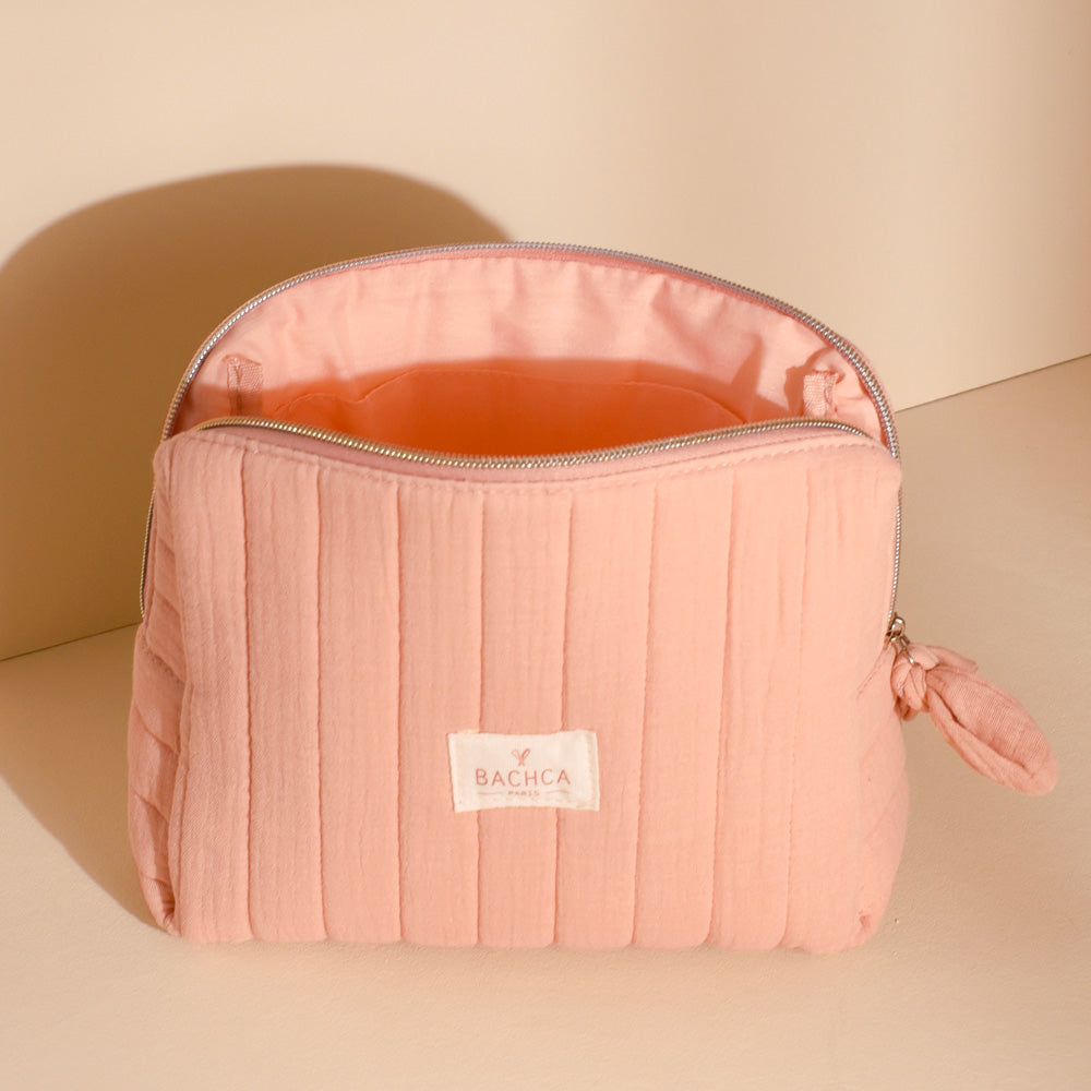 Trousse de toilette Bachca en coton matelassé rose poudré ouverte, avec intérieur spacieux et fermeture éclair, posée sur fond nude.