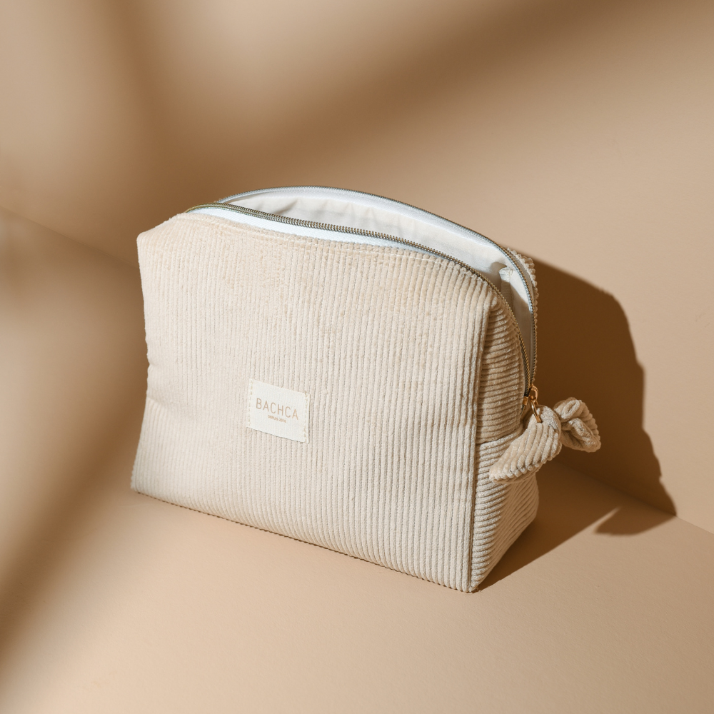 Trousse de toilette BACHCA en velours beige sable, posée sur fond sable, lumière douce et naturelle.