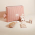 Trousse rose Bachca et accessoires assortis : brosse en bois, pinces guiches, élastiques et barrette ronde.