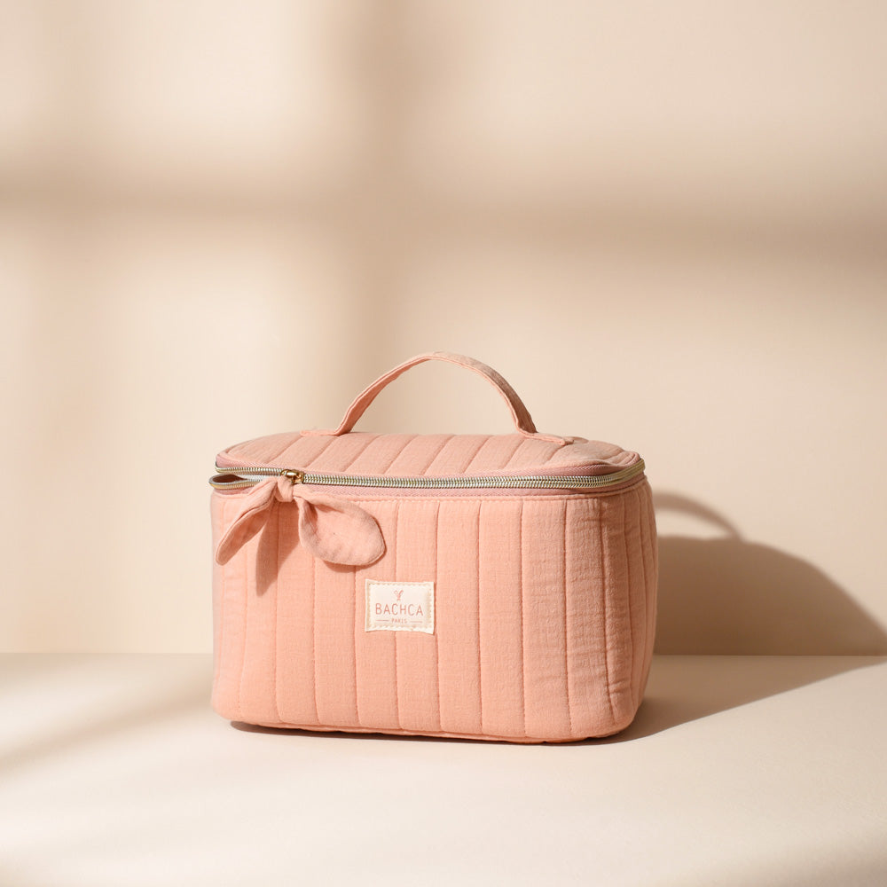 Vanity rectangulaire Bachca matelassé en coton rose poudré avec fermeture éclair dorée et petite anse, posé sur un fond beige lumineux.