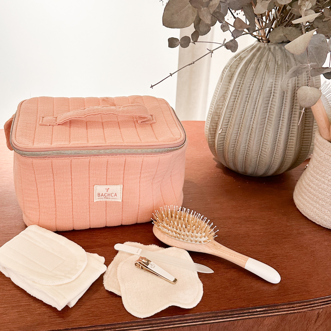 Vanity rose Bachca accompagné d'une brosse cheveux, de cotons lavables, d'une lime en verre et d'un coupe-ongles, sur meuble en bois.