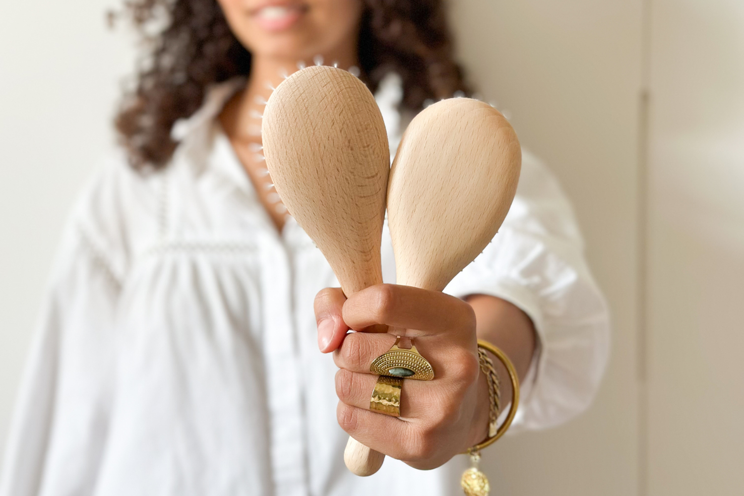 Gros plan sur deux brosses à cheveux en bois de hêtre de la marque Bachca présentées dans les mains d'une femme souriante en arrière plan.