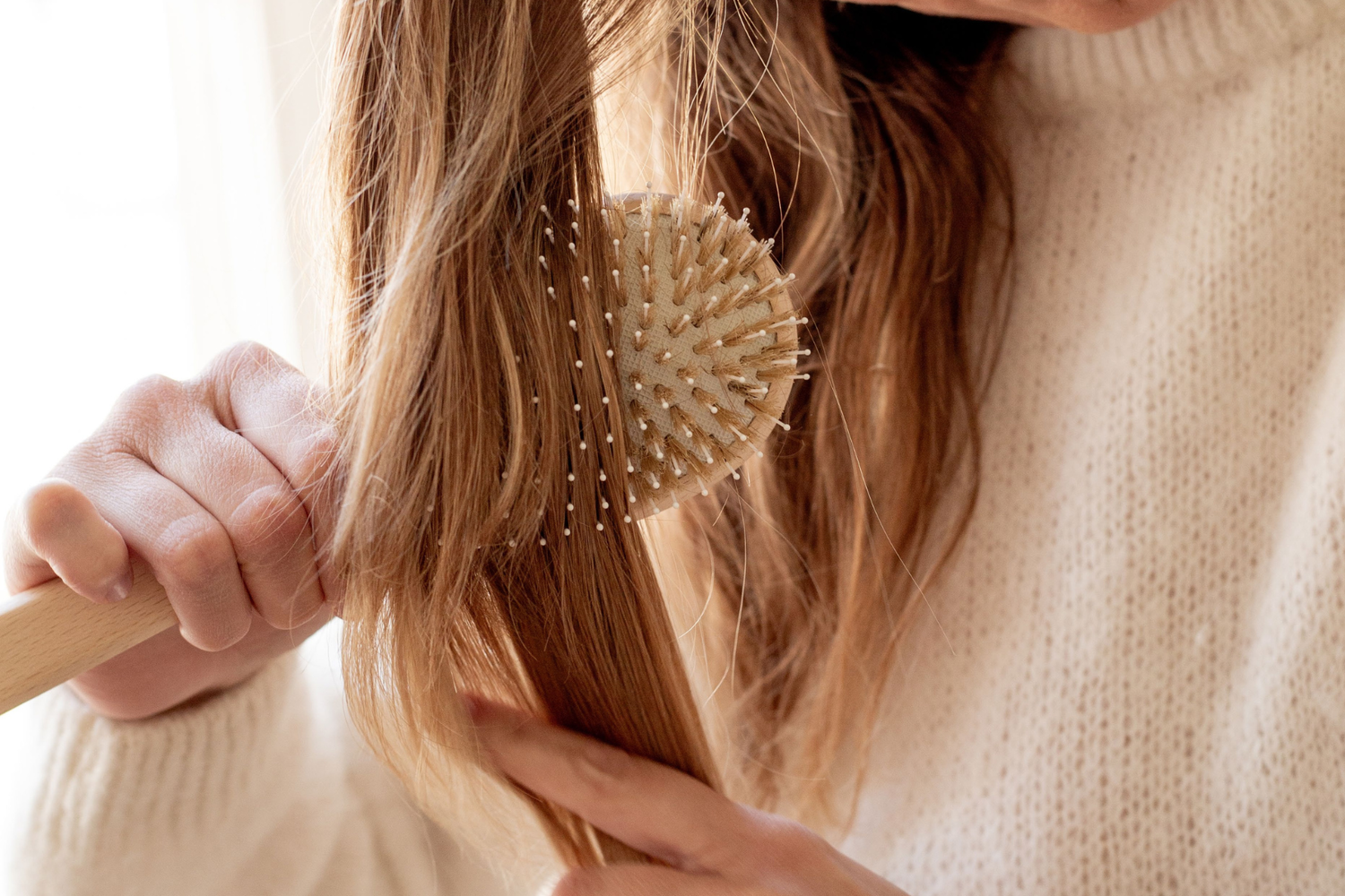 Zoom sur une femme utilisant une brosse à cheveux de la marque Bachca, gros plan sur la pneumatique de la brosse, couleurs chaudes et pâles.