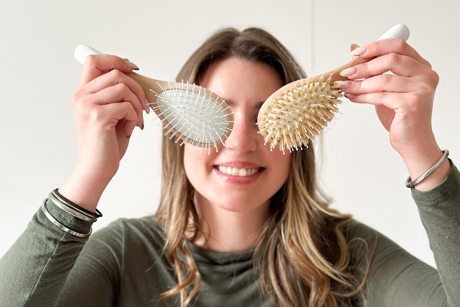 Jeune femme souriante qui tient dans ses mains deux brosses à cheveux différentes de la marque Bachca.
