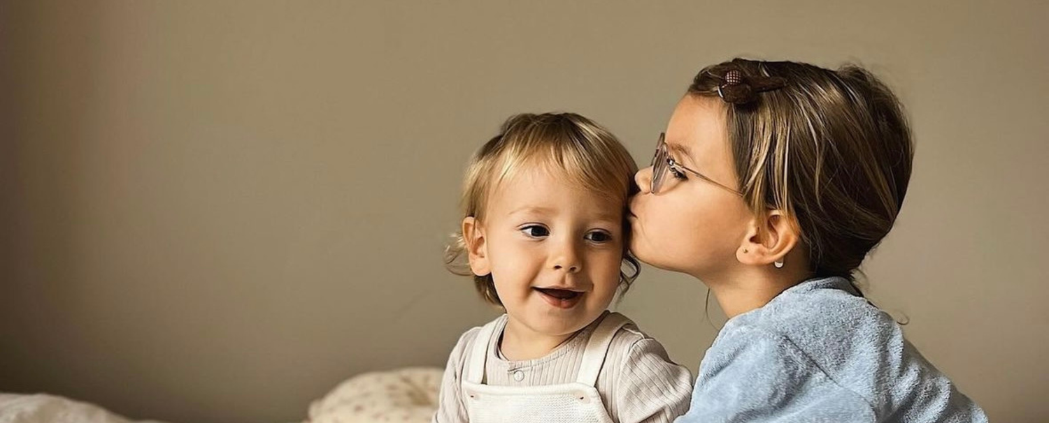 Photo d'une petite fille faisant un bisou sur le front de son petit frère.