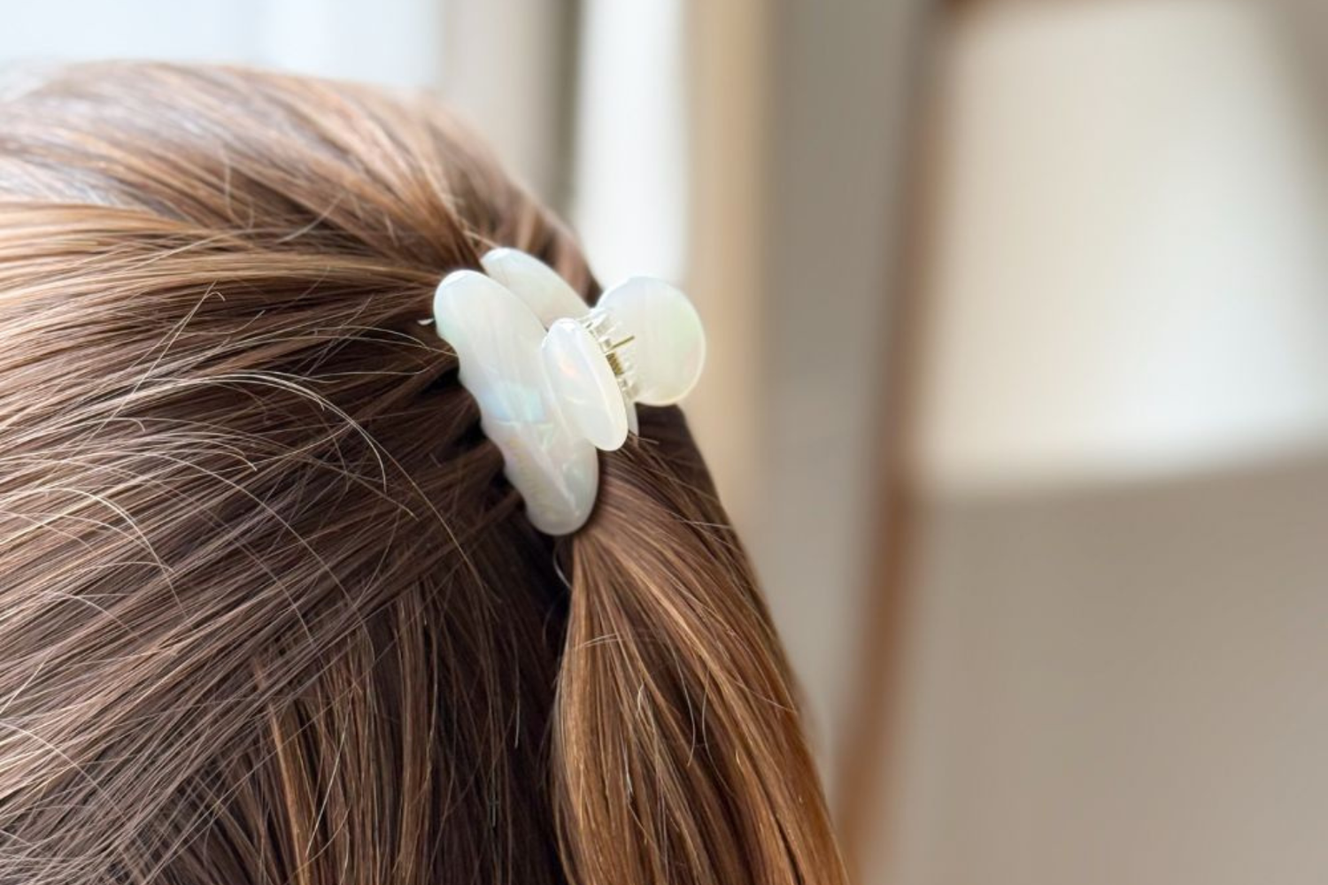 Zoom sur une petite pince à cheveux nacrée de la marque Bachca qui coiffe des cheveux bruns en demi-queue.