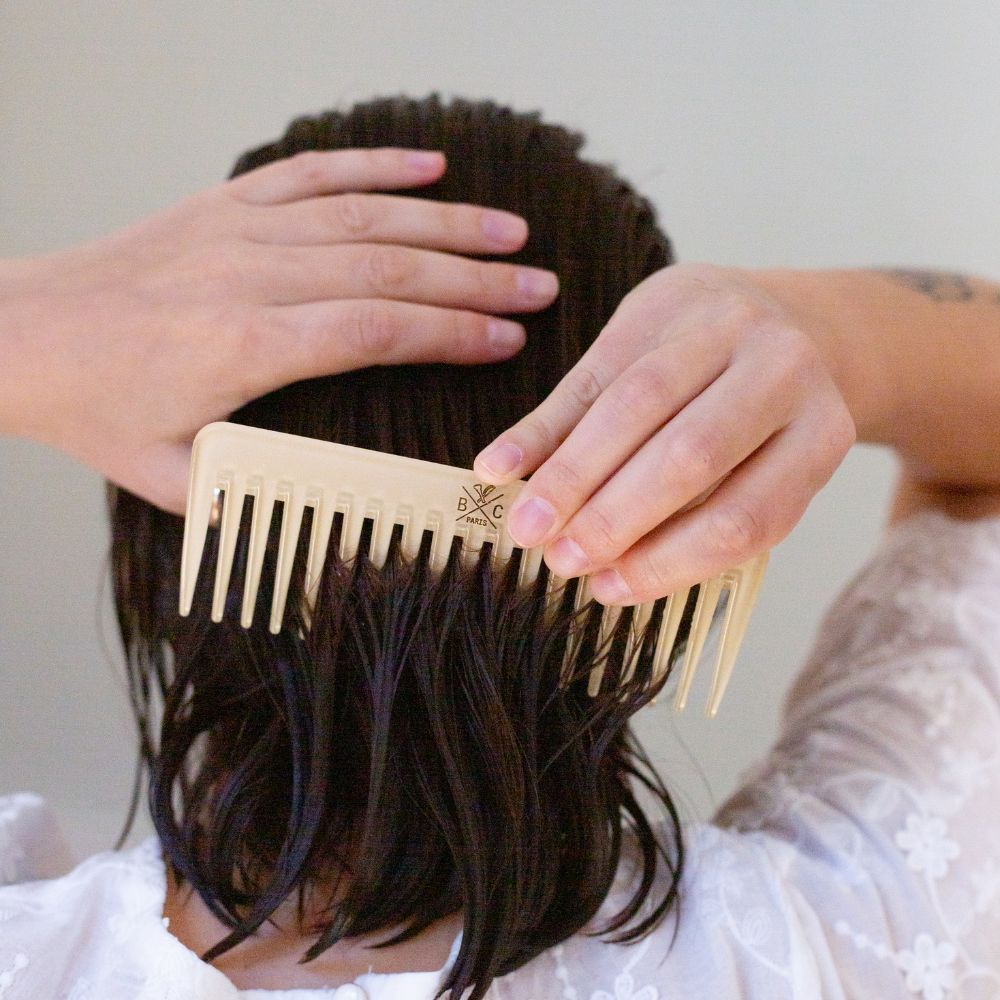 Femme coiffant ses cheveux mouillés avec un peigne à larges dents Bachca en acétate d'opaline, idéal pour démêler sans casser la fibre.