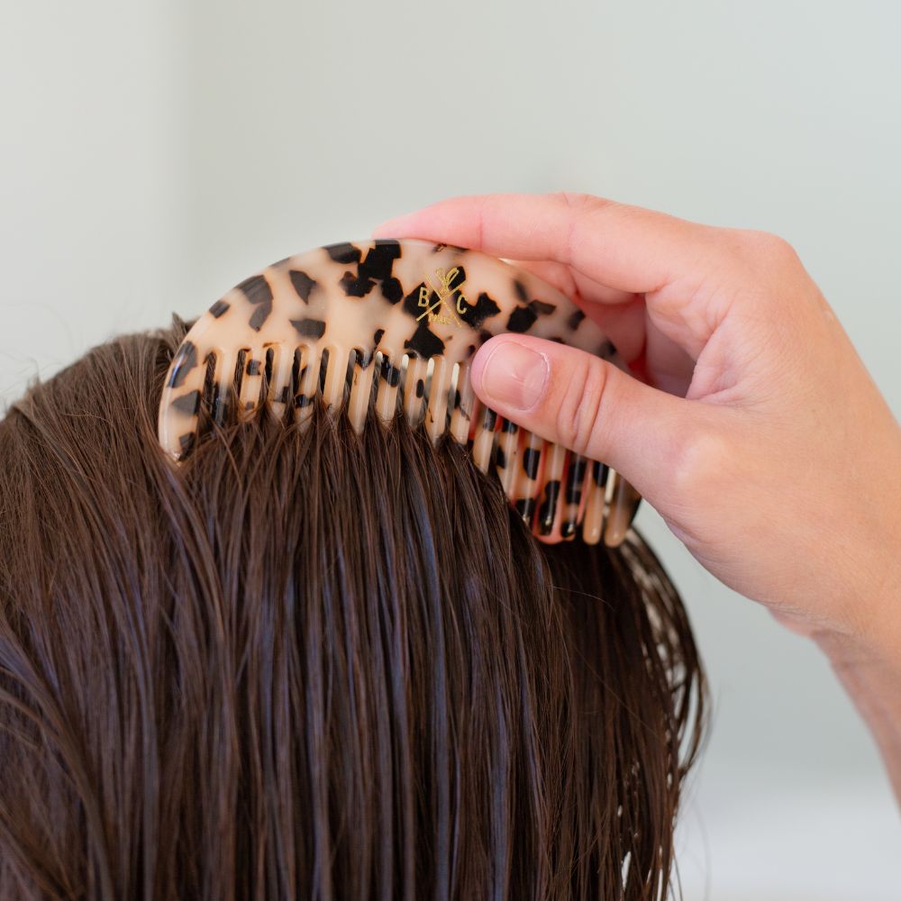 Main coiffant des cheveux mouillés avec un grand peigne Bachca en acétate effet écaille, aux dents larges, parfait pour démêler en douceur.