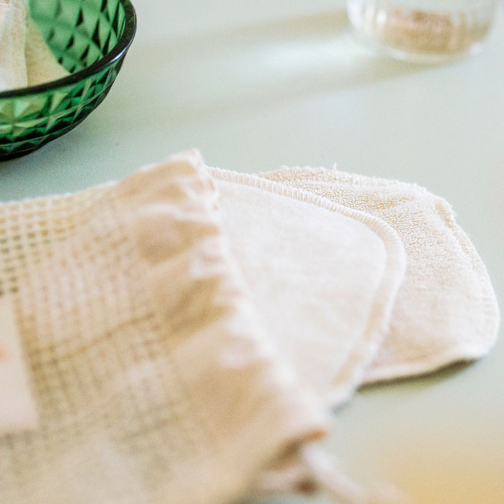 Lot de cotons démaquillants lavables Bachca en coton doux beige, posés avec leur pochette filet réutilisable.