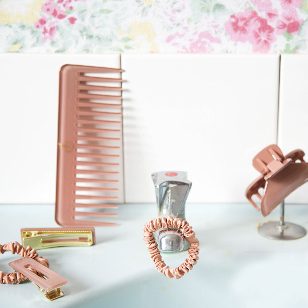 Accessoires cheveux Bachca en terracotta posés dans une salle de bain : peigne, pinces et chouchous.