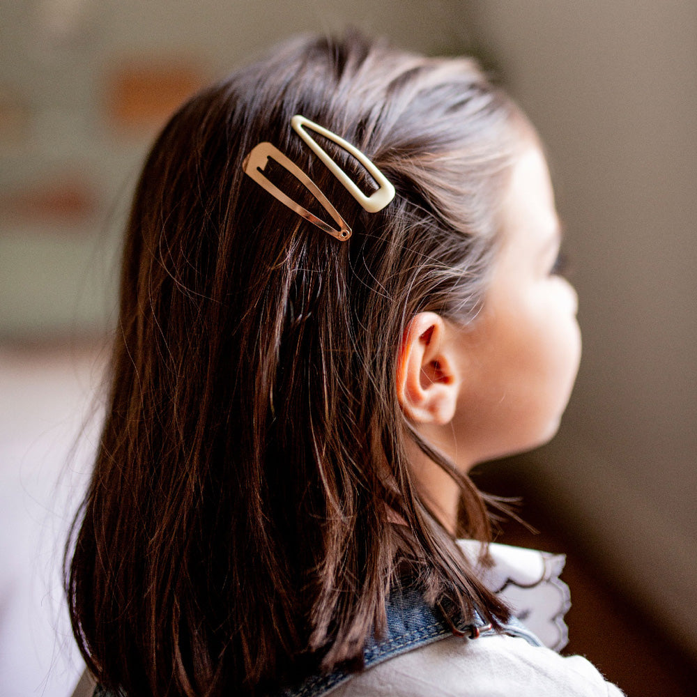 Petite fille portant deux barrettes Bachca en métal doré et ivoire, idéales pour attacher les cheveux avec élégance et simplicité.