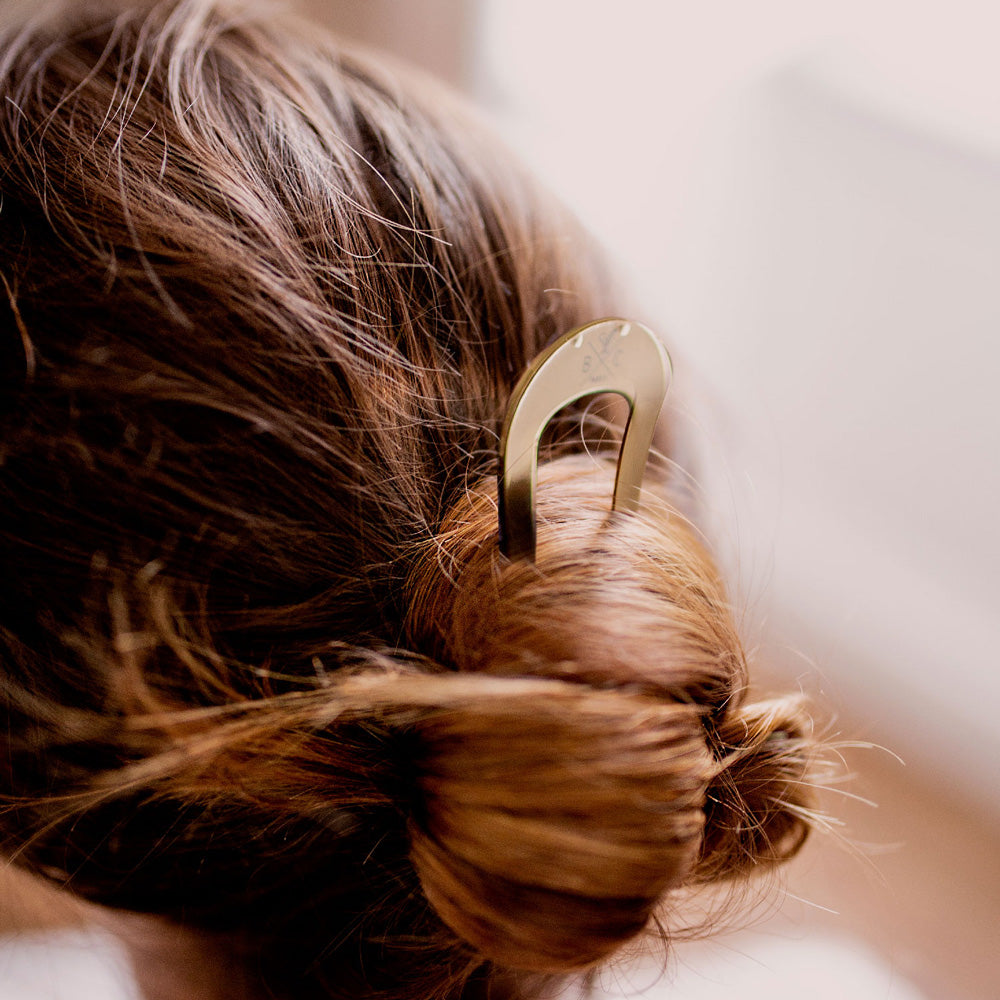 Chignon bas maintenu avec un pic à chignon doré Bachca, accessoire coiffure chic et pratique pour cheveux longs.