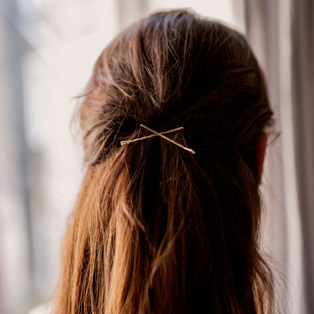 Cheveux attachés à l’arrière avec deux pinces guiches dorées Bachca croisées, accessoire discret et élégant pour maintenir les mèches en toute simplicité.