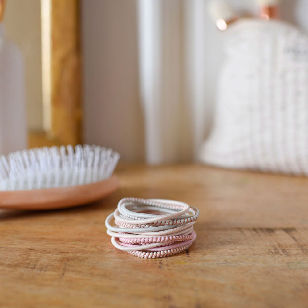 Élastiques à cheveux Bachca en tons pastel rose et beige, présentés sur une coiffeuse en bois avec une brosse en arrière-plan, accessoires coiffure élégants et résistants.