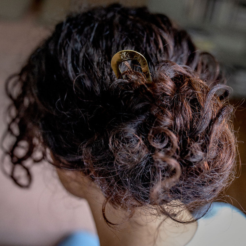 Chignon flou maintenu avec un pic à chignon doré Bachca, accessoire élégant et pratique pour cheveux bouclés ou épais.