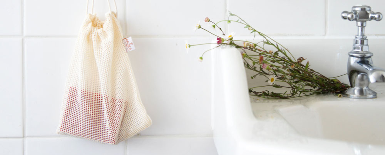Photo lifestyle qui met en avant le filet à savon de la marque Bachca à côté d'un lavabo de salle de bain décoré d'un petit bouquet de fleurs bucolique.