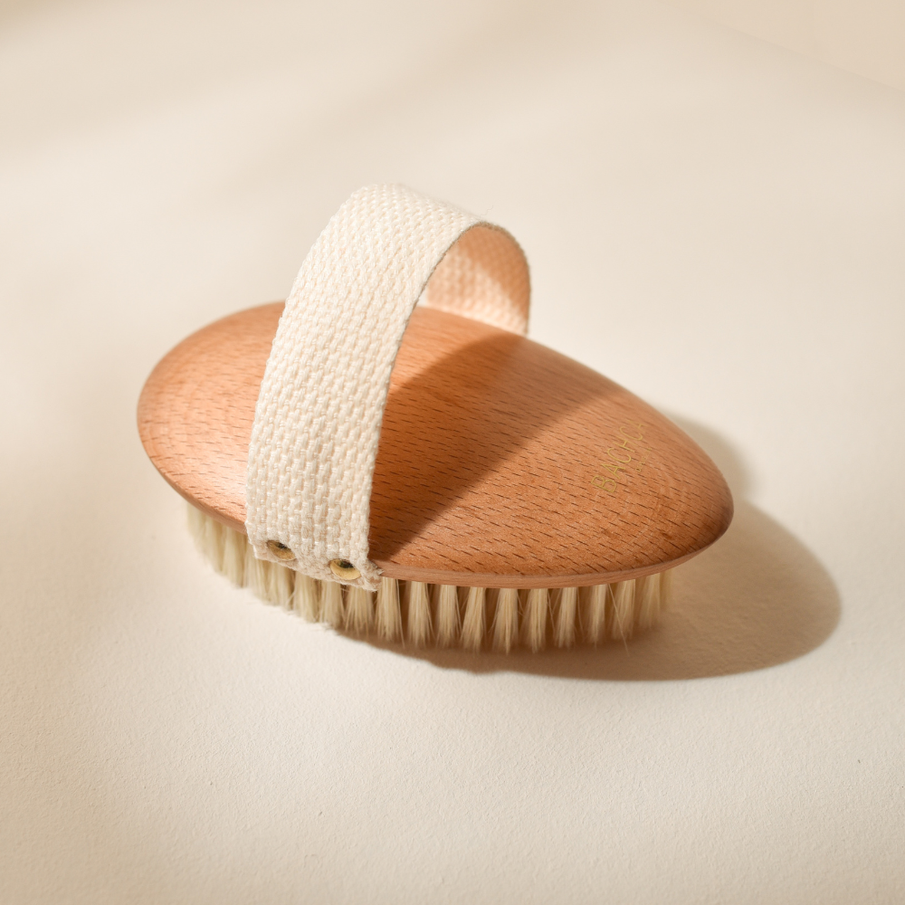 Photo studio sur fond beige, le produit mis en avant est la brosse de massage à sec Bachca, la brosse est en bois de hêtre, les poils sont en soie de sanglier.