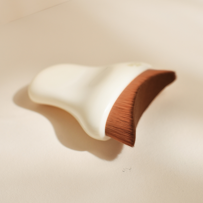 Photo studio sur fond beige, la brosse visage de drainage lymphatique Bachca est posée sur le fond, on peut ainsi voir sa forme rectangulaire et ses poils synthétiques.