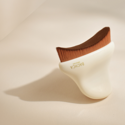 Photo studio sur fond beige, la brosse de drainage lymphatique visage Bachca est mise en avant. La brosse est triangulaire, avec des poils doux et un manche en acétate de cellulose.