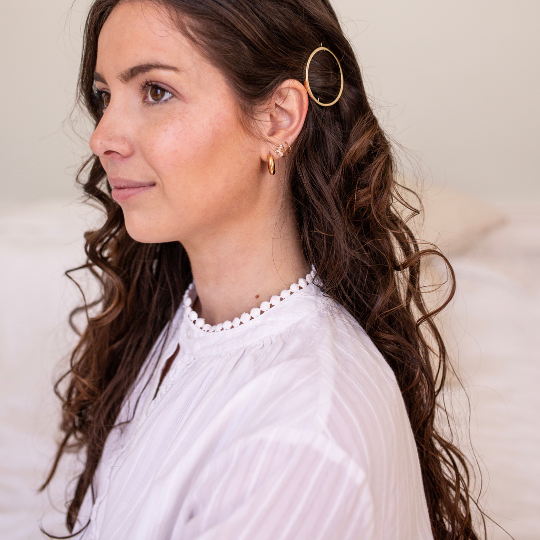 Femme aux cheveux bruns ondulés portant une barrette ronde dorée Bachca, coiffure élégante et naturelle.