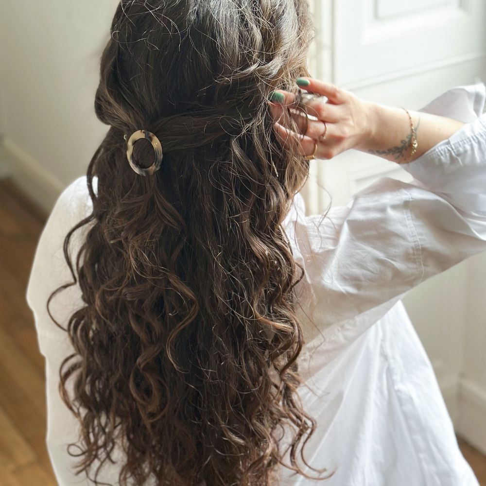 Cheveux longs et bouclés attachés en demi-queue avec une barrette ronde écaille Bachca élégante.