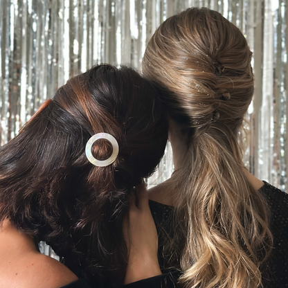 Deux femmes sont de dos, elles portent dans les cheveux des accessoires de la marque Bachca, on peut voir en arrière plan un fond argenté festif.