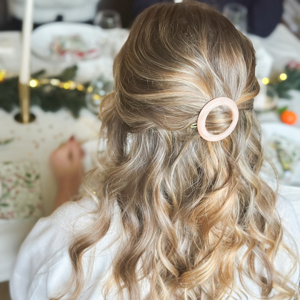 Une femme de dos assise à une table, elle porte dans ses cheveux une barrette ronde rose de la marque Bachca, la table à manger est décorée pour noël.
