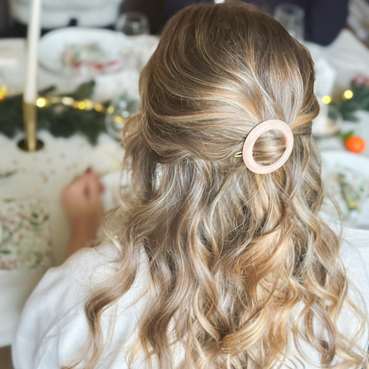 Une femme de dos assise à une table, elle porte dans ses cheveux une barrette ronde rose de la marque Bachca, la table à manger est décorée pour noël.